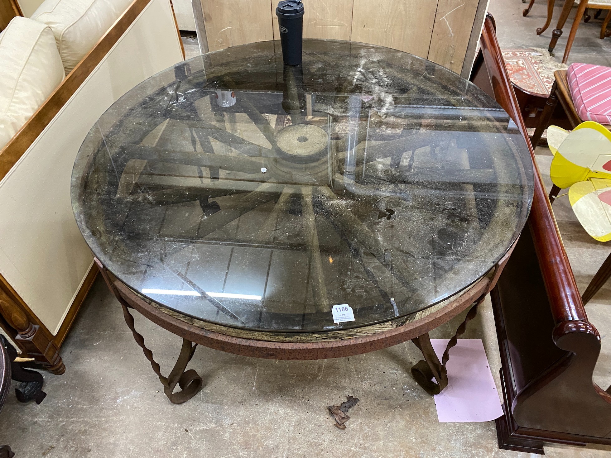 A wrought iron glass topped circular cartwheel garden table, diameter 124cm, height 72cm